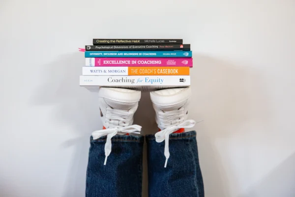 Ashfold Consulting – Linda’s Approach to Coaching A stack of coaching books against a wall being held up by some upside down trainers.