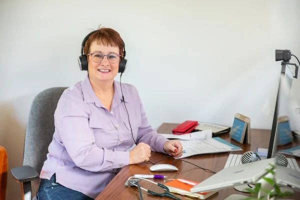 Linda Gent at a desk with headphones on, looking at the camera and smiling
