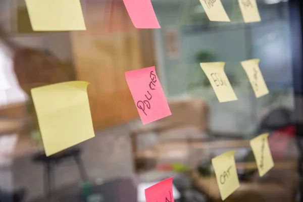 A glass wall with post its on it. The post it closest to the shot reads policies
