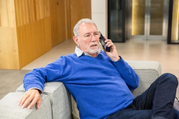 Andrew Gent sitting on a sofa in an office, while speaking on the phone.